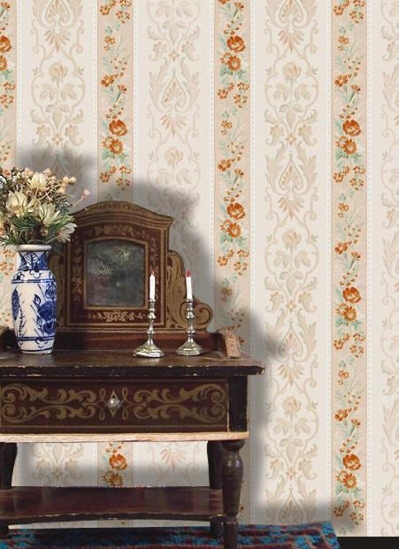 Puede incluir: Una escena de estilo vintage con una mesa de madera, un espejo y candelabros. Un jarr&oacute;n azul y blanco con flores est&aacute; sobre la mesa. El fondo es un papel pintado crema con motivos florales y damasco.