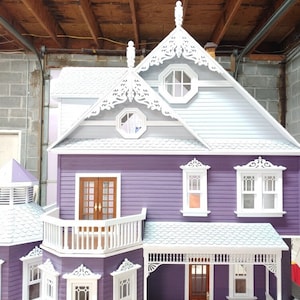 May include: A purple and white dollhouse with a detailed exterior, including a balcony, porch, and decorative trim. The roof is white with a gray shingle pattern.