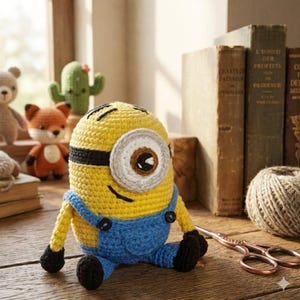 May include: A handmade crochet Minion toy in yellow and blue. The Minion has a large, single eye, black hair, and is wearing blue overalls. Other crochet toys, books, and scissors are in the background.
