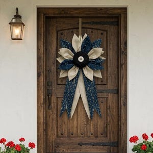 May include: A decorative door wreath shaped like a large flower with alternating petals made of beige burlap and navy blue fabric with a small floral pattern. The center of the flower is a black circular piece with a white button in the middle.