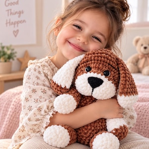 Puede incluir: Un perro de peluche hecho de hilo grueso marrón y blanco. El animal de peluche presenta una cabeza redonda marrón, orejas caídas blancas y marrones, un hocico blanco con una nariz negra y patas blancas. La textura es suave y esponjosa.