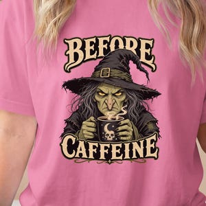 May include: A pink short-sleeved t-shirt featuring a graphic of a witch wearing a pointed hat and holding a mug with a skull design. The text above the witch reads BEFORE and the text below reads CAFFEINE. The shirt is paired with black leggings.