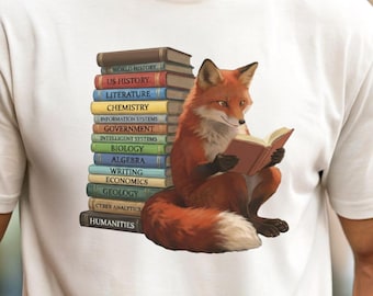 May include: A cream-colored short-sleeve t-shirt featuring a graphic of a red fox sitting beside a tall stack of colorful books. The fox is holding an open book. The book spines are labeled with subjects including US History, Literature, Chemistry, Biology, Algebra, Writing, Economics, Geology, and Humanities.