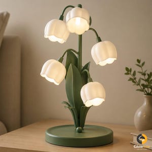 May include: A green lily-of-the-valley table lamp with five white flower-shaped shades. The lamp has a round base and a central stem with leaves. The lamp is on a wooden surface.