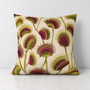 May include: A square throw pillow featuring a cream-colored background with a repeating botanical pattern of Venus flytrap plants. The plants have vibrant green stems and leaves with deep red, toothy traps arranged in various open positions.