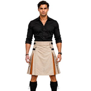 May include: A tan kilt with brown accents and black details. The kilt has pockets and a logo on the front. The person is wearing a black button-down shirt and black boots.