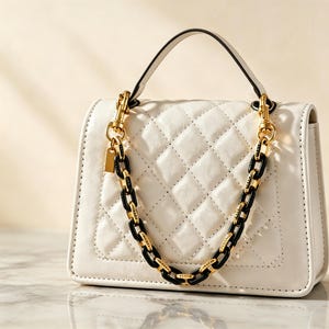 May include: A white quilted handbag featuring a top handle and a decorative chain strap composed of alternating gold-tone metal and black links. The bag has a structured rectangular shape with a flap closure and a small gold-tone metal tag.