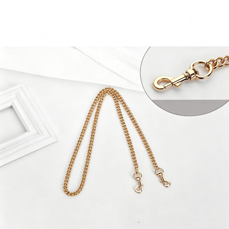 May include: A gold-toned metal chain strap featuring a curb link design. The strap includes two swivel lobster claw clasps at the ends for attachment. A circular inset shows a detailed view of the metal clasp mechanism connected to the chain links.