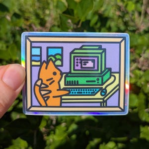 Puede incluir: Una pegatina holográfica rectangular con una ilustración de dibujos animados de un gato naranja sentado en un escritorio usando una computadora antigua. La escena incluye una pared morada, un teclado, un ratón y dos ventanas con cielo azul.