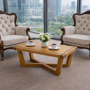 May include: Two upholstered armchairs with dark wood trim flank a wooden coffee table. The table has a cross-legged base and a rectangular top. Two cups of coffee and a vase of white flowers sit on the table. The chairs have button-tufted backs.