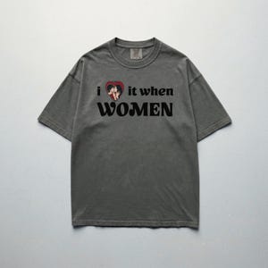 May include: Gray t-shirt with the text "i ❤️ it when WOMEN". The heart graphic features two figures. The shirt has short sleeves and a crew neck.