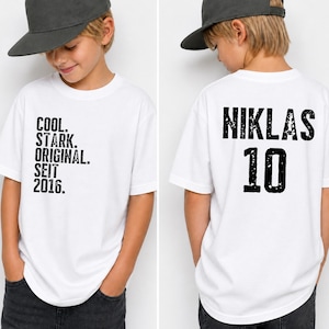 Könnte beinhalten: Ein weißes T-Shirt mit kurzen Ärmeln und schwarzem, abgenutztem Text auf der Vorderseite: COOL. STARK. ORIGINAL. SEIT 2016. Auf der Rückseite steht der Name NIKLAS in schwarzer, abgenutzter Schrift über der großen schwarzen Zahl 10.