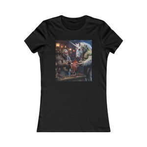 May include: Black t-shirt featuring a fantasy scene of a Bigfoot-like creature and a unicorn examining a leather item in a workshop setting. The image has a detailed, artistic style with warm lighting.