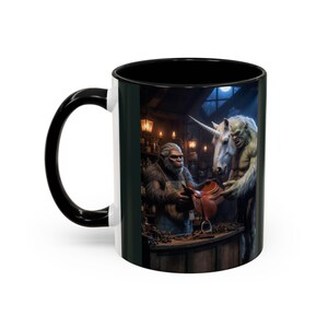 May include: A white ceramic mug with a black handle and interior. The mug features a fantasy scene of a Bigfoot-like creature and a muscular unicorn-like creature in a workshop. The Bigfoot-like creature is holding a saddle.