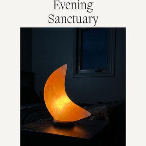 May include: A crescent moon-shaped salt lamp emitting a warm orange glow, resting on a dark circular base. The text 'Create Your Evening Sanctuary' appears above the lamp, and 'MADE2GLOW GIFTS' is printed at the bottom of the image.