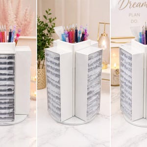 May include: A white, rotating organizer with multiple compartments for storing craft supplies. The organizer has a circular base and a top section for holding pens and brushes. The compartments are filled with small, clear containers. The organizer is designed to hold various art supplies.