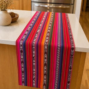 May include: A vibrant, striped table runner in shades of red, pink, orange, blue, and green. The runner features intricate geometric patterns along the edges. This decorative textile adds a pop of color to any dining or living space.