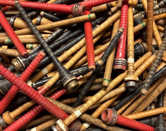 May include: A box full of wooden bobbins in red, black and natural wood tones. The bobbins are used for spinning yarn.