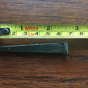 May include: A black metal nail measuring approximately 2 inches in length. The nail is shown next to a yellow measuring tape with the text "12 FEET 3.5m" printed on it.