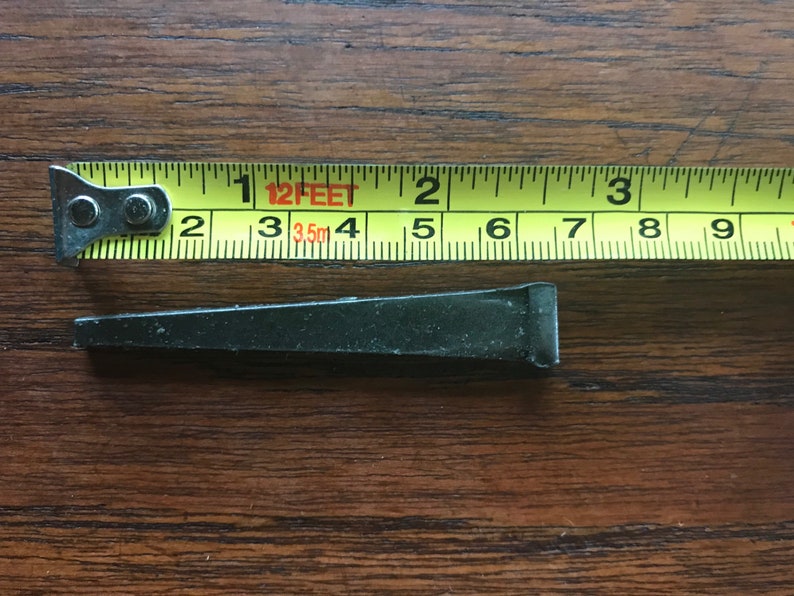 May include: A black metal nail measuring approximately 2 inches in length. The nail is shown next to a yellow measuring tape with the text "12 FEET 3.5m" printed on it.