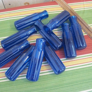 May include: A group of ten cobalt blue glass bottles with a ribbed texture. The bottles are arranged in a random pattern on a striped fabric surface.
