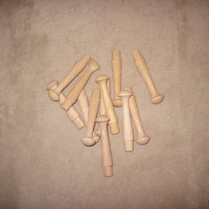 May include: A group of wooden dowels with rounded ends, arranged in a loose pile on a brown surface.
