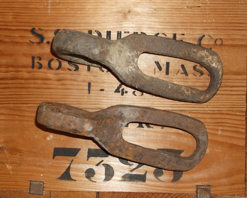 K&ouml;nnte beinhalten: Zwei rostige Metallringe mit abgerundeter Kante und ovaler &Ouml;ffnung. Die Ringe liegen auf einer Holzoberfl&auml;che mit schwarzem Text, der "S.G. PIERCE CO. BOSTON, MASS. 1-48 7529" lautet.