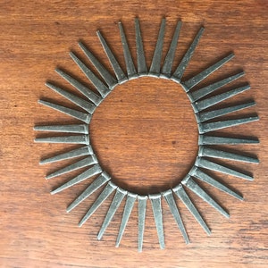 May include: A circular arrangement of silver-colored nails, forming a sunburst pattern on a wooden surface.