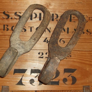 K&ouml;nnte beinhalten: Zwei rostige Metallhaken mit abgerundeter Oberseite und spitzer Unterseite. Die Haken liegen auf einer Holzoberfl&auml;che mit schwarzen Zahlen und Buchstaben. Die Buchstaben lauten "S.S. PIERCE CO BOSTON MASS 46 22 725".