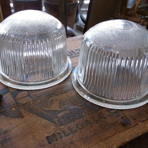 May include: Two clear glass dome-shaped lampshades with ribbed detailing. The lampshades are sitting on a wooden surface.