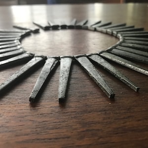 May include: A circular arrangement of silver-colored metal nails, arranged in a sunburst pattern on a dark wood surface.