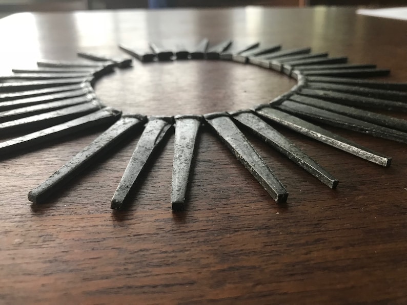 May include: A circular arrangement of silver-colored metal nails, arranged in a sunburst pattern on a dark wood surface.