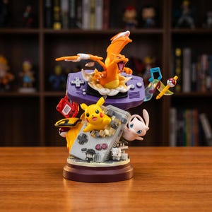 Peut inclure: Figurine détaillée représentant plusieurs personnages Pokémon, dont Dracaufeu, Pikachu et Mew, disposés autour d'une console de jeu violette. La figurine a une base marron et est placée devant une bibliothèque floue.