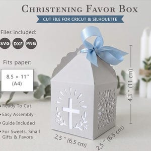 May include: A light grey Christening favour box with a cross design and a light blue ribbon. The box is 6.5 cm wide and deep, and 11 cm tall. The text on the box says "Christening Favor Box".