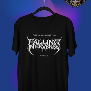 以下が含まれることがあります： 黒いTシャツ。白いスタイリッシュなフォントで「FALLING IN REVERSE」のバンド名がプリントされ、その上に「POPULAR MONSTER」、下に「NO FEAR」の文字。Tシャツは黒いハンガーに掛けられています。