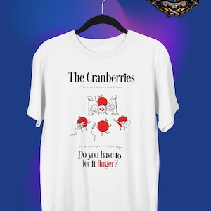 May include: White t-shirt with "The Cranberries" band name and lyrics. The design features cartoon red fruit characters playing instruments. The text "Do you have to let it linger?" is also displayed.
