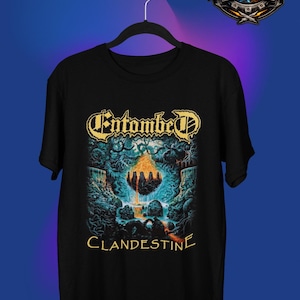 Puede incluir: Camiseta negra con el nombre de la banda "Entombed" en letras doradas sobre un gráfico detallado de un paisaje surrealista con una roca flotante y la palabra "Clandestine" debajo.