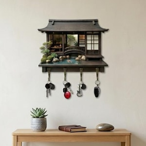 Könnte beinhalten: Ein dunkelbrauner Wand-Schlüsselhalter mit einem Miniaturgebäude im japanischen Stil, einer Brücke, einem kleinen Teich und Grünpflanzen. Die Struktur verfügt über vier Metallhaken an der Unterseite, an denen jeweils Schlüssel hängen.