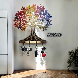 Könnte beinhalten: Ein mehrfarbiger Baum-Schlüsselhalter mit Holzsockel und Haken. Die Blätter des Baumes zeigen einen Regenbogen an Farben. Das Wort "SANDWOOD" ist an der Wand zu sehen. Mehrere Schlüssel hängen an den Haken.