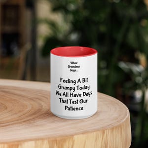 Puede incluir: Una taza de cerámica blanca con un interior de color rojo brillante. El exterior presenta un texto impreso en negro que dice: What Grandma Says... Feeling A Bit Grumpy Today We All Have Days That Test Our Patience. La taza es cilíndrica.