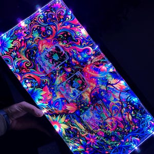 Könnte beinhalten: Ein rechteckiges, beleuchtetes Kunstwerk mit einem lebendigen, psychedelischen Blumendesign. Das Kunstwerk zeigt einen schwarzen Hintergrund mit neonfarbenen rosa, blauen, grünen und gelben Blumen und Blättern. Die Kanten sind mit kleinen, hellweißen Lichtern versehen.