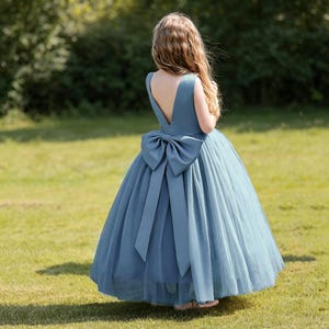 May include: A blue formal dress with a large bow on the back. The dress has a V-neck and a full skirt made of tulle. The dress is suitable for a flower girl or special occasion.