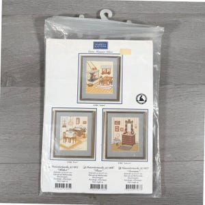 May include: A clear plastic package containing a Marks & Kattens cross-stitch pattern kit. The insert displays three framed interior scenes: a kitchen, a dining room, and a bedroom. Each design features detailed furniture and decor in warm tones.