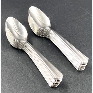May include: A collection of shiny, silver spoons arranged in two stacks. The spoons have a classic design with a rounded bowl and a ridged handle. The spoons are made of a reflective metal, likely stainless steel, and are set against a dark background.