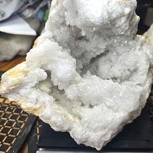 May include: A large, jagged white quartz geode with a hollow, crystalline interior resting on a digital scale. The scale display shows a weight of 6 pounds and 6.8 ounces. The exterior of the rock is rough, textured, and tan in color.