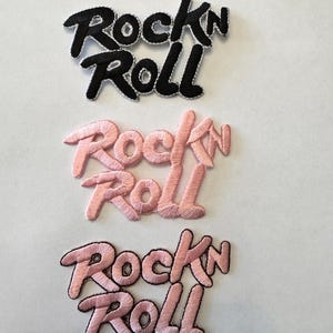 May include: Three embroidered iron-on patches with the words "Rock'n Roll" in black and pink. The patches are arranged vertically, with the black patch at the top and the two pink patches below.