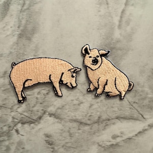 May include: Two embroidered patches of pink pigs. One pig is standing and the other is sitting.