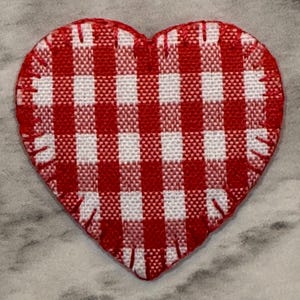 May include: A red and white gingham heart-shaped patch. The patch has a stitched edge and a classic checkered pattern. The heart is a vibrant red and white, perfect for crafts or adding a touch of charm.