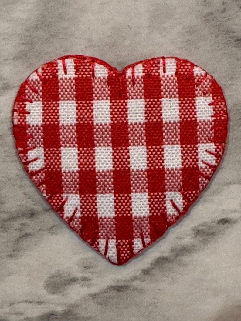 May include: A red and white gingham heart-shaped patch. The patch has a stitched edge and a classic checkered pattern. The heart is a vibrant red and white, perfect for crafts or adding a touch of charm.