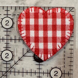 May include: A red and white gingham heart-shaped fabric patch. The patch is approximately 2 inches wide and is placed on a clear ruler with black markings and the number 2.